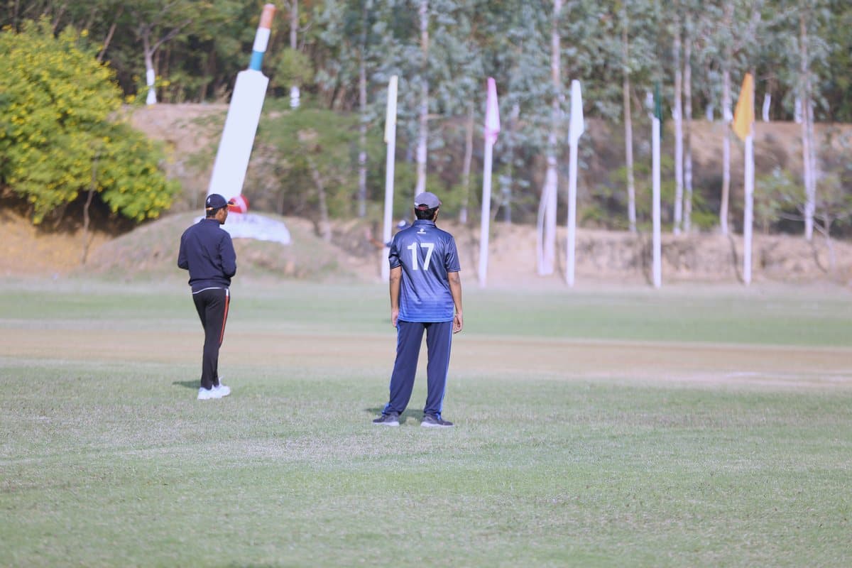 The umpire and a fielder at the giant bat monument, flags along the boundary