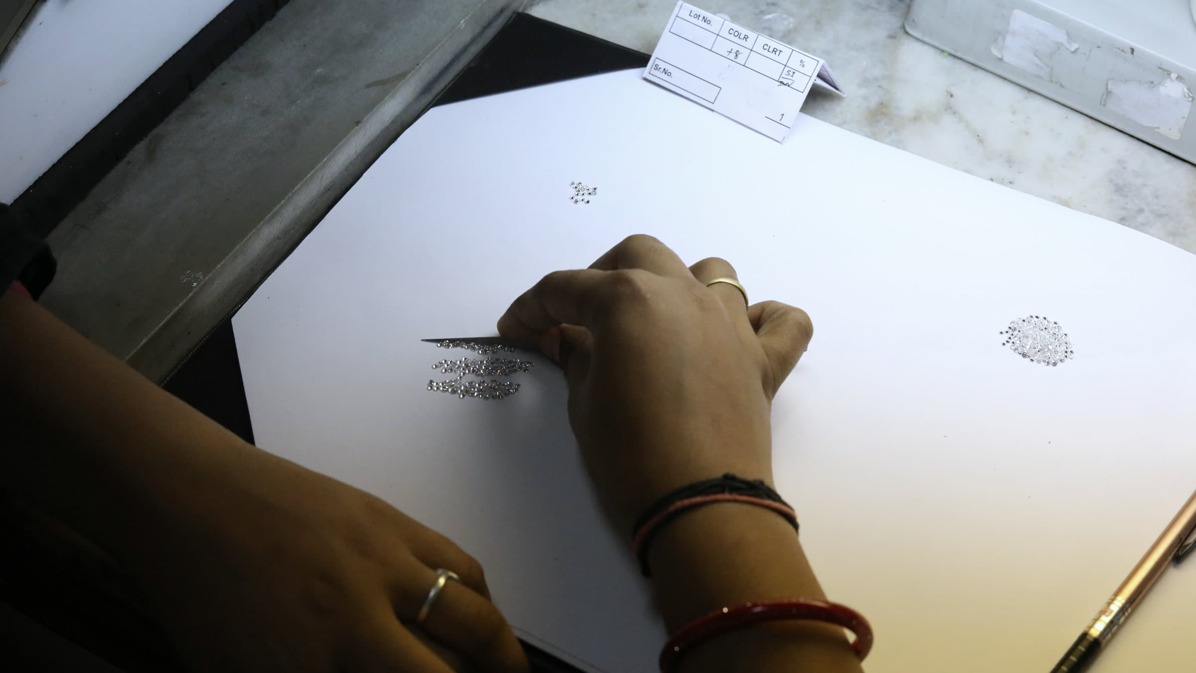 A hand sorting small stones on a white pad beside a lot sheet