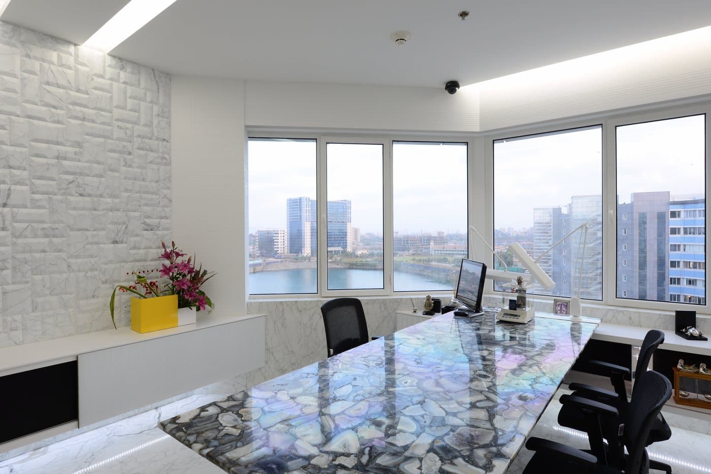 An office with an agate-top desk, marble wall, flowers and the city and lake beyond the window